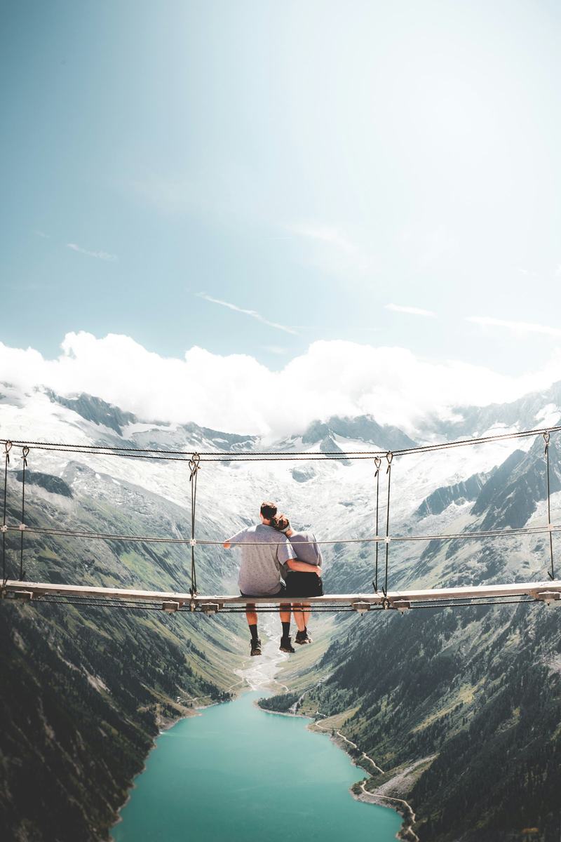 Two travellers on a suspension bridge above a mountain lake