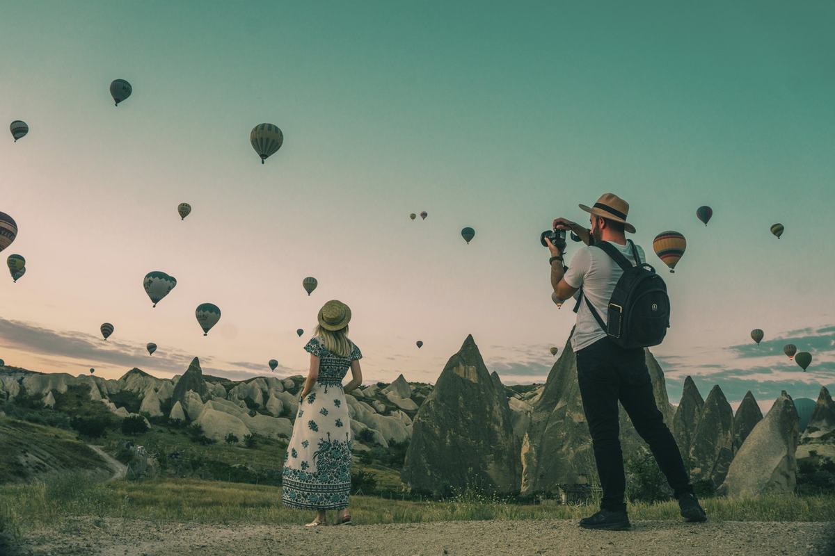 Travellers photographing hot-air balloons at sunrise
